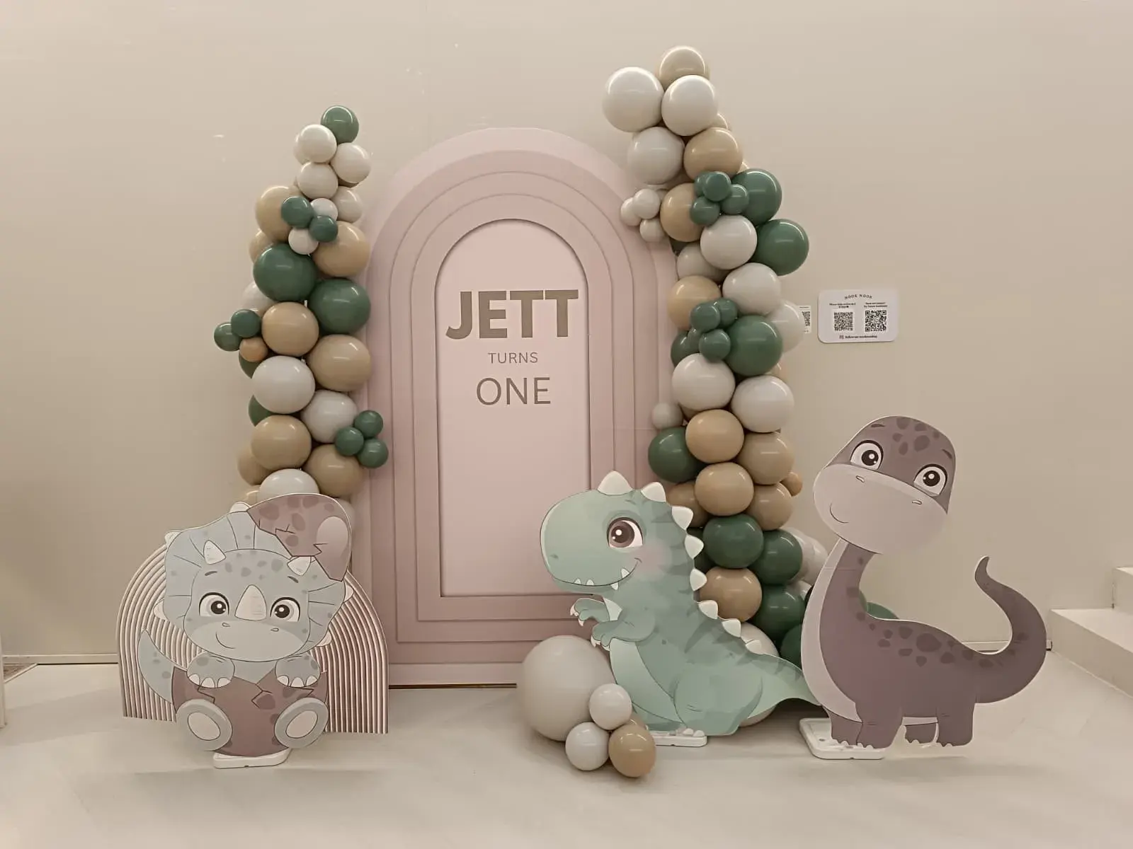 A dinosaur themed first birthday backdrop with a balloon garland